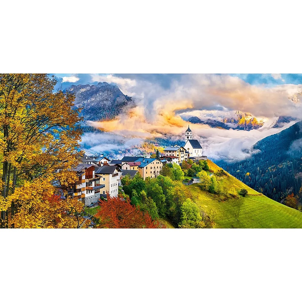 Alpines Dorf im Herbst mit gelben Bäumen, Kirche auf dem Hügel und nebligen Bergen im Hintergrund.