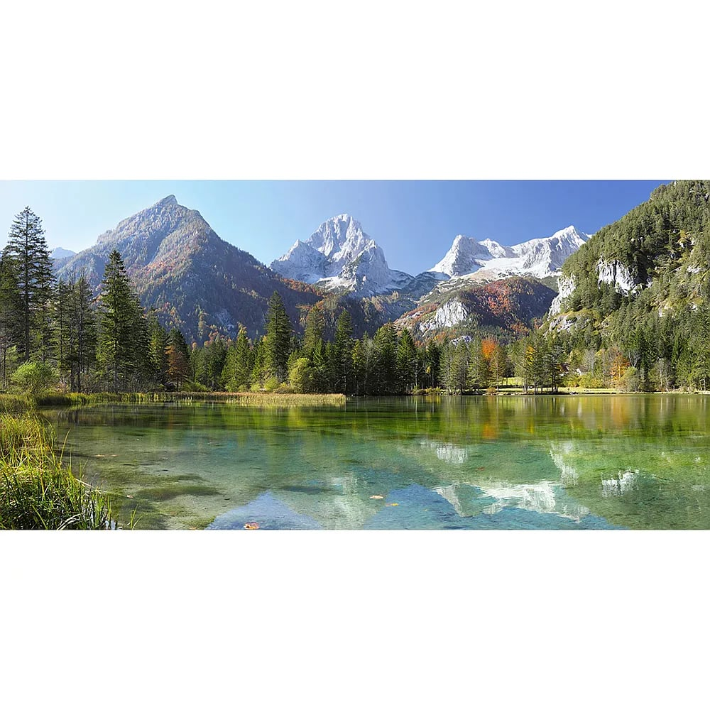 Ein klarer Bergsee spiegelt majestätische schneebedeckte Gipfel und grüne Wälder unter blauem Himmel wider.