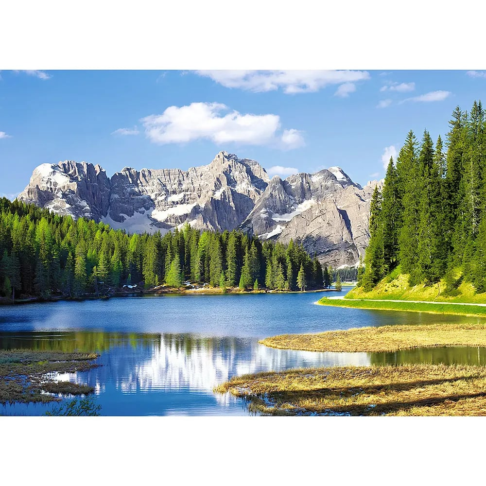 Ein blauer Bergsee mit dichten grünen Nadelwäldern und schroffen, schneebedeckten Bergen im Hintergrund unter klarem Himmel.