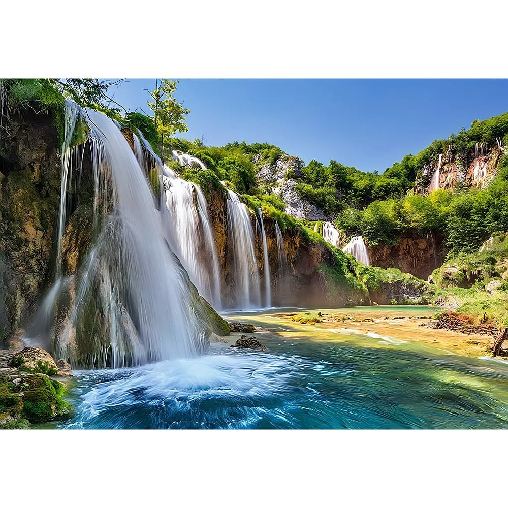 Fließende Wasserfälle stürzen in einen klaren, türkisblauen See, umgeben von üppigem grünem Wald unter einem blauen Himmel.