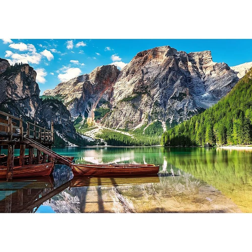 Holzboote an einem klaren Bergsee vor majestätischen, felsigen Bergen und blauem Himmel mit Wolken.