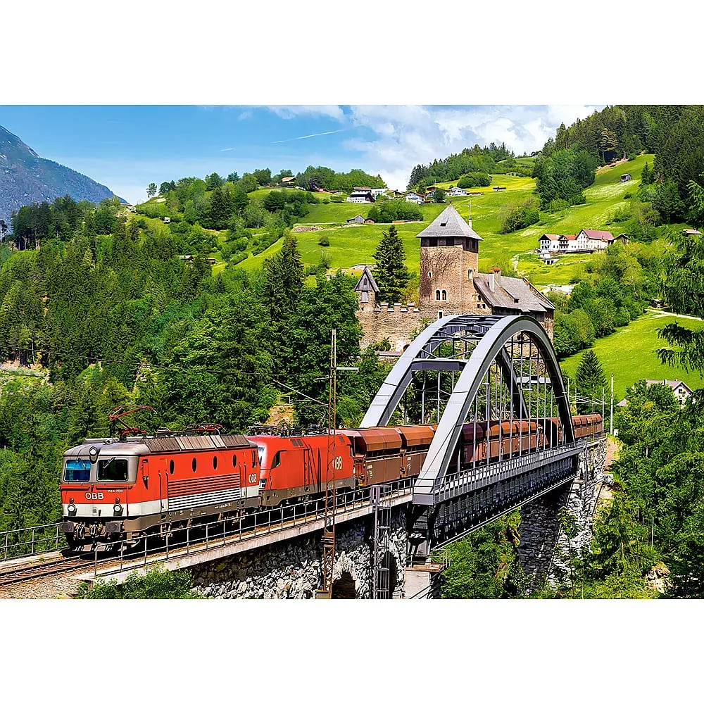 Ein roter Güterzug überquert eine Bogenbrücke in einem grünen Tal mit einer Steinburg.