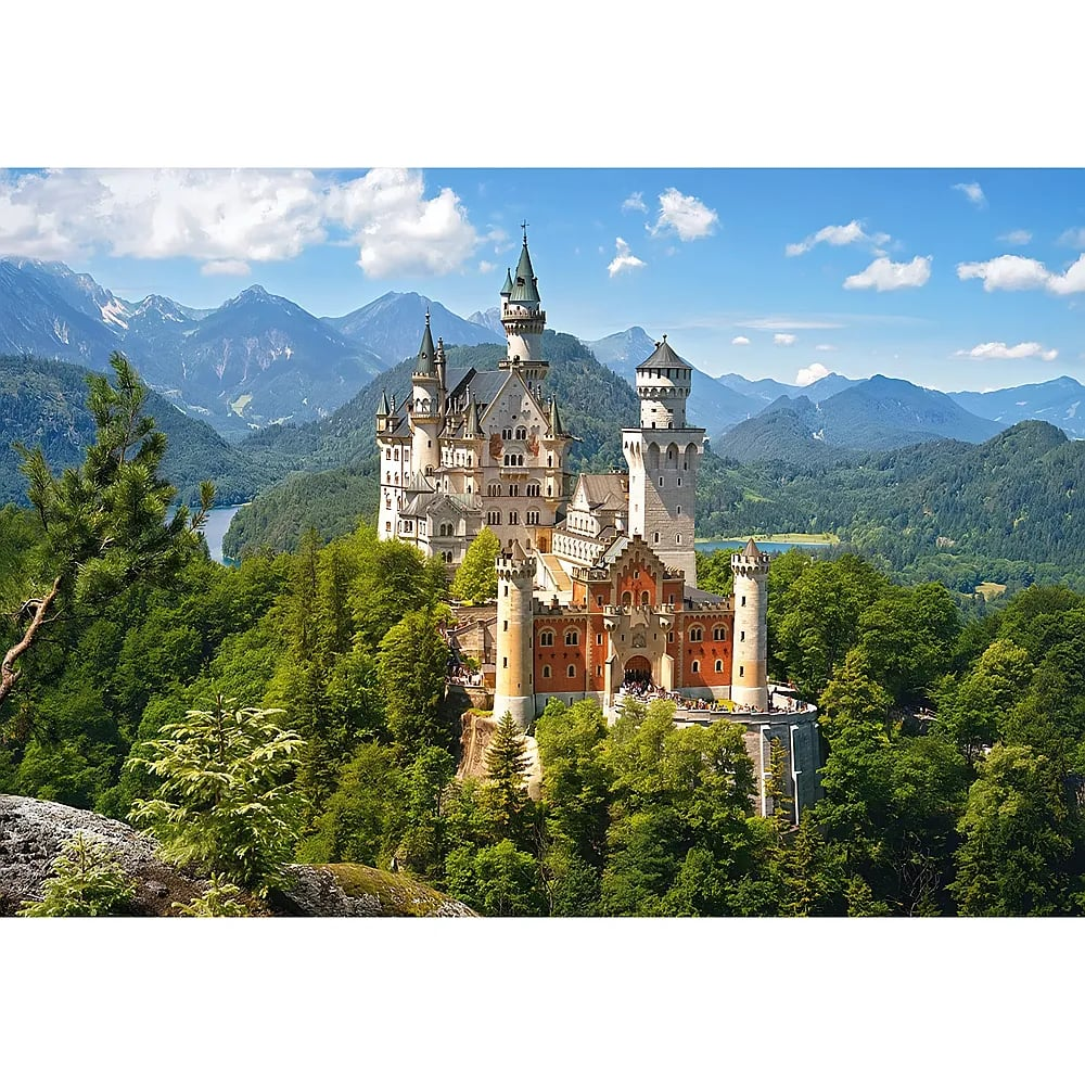 Le château de Neuschwanstein sur des collines boisées avec en fond des montagnes majestueuses sous un ciel bleu.