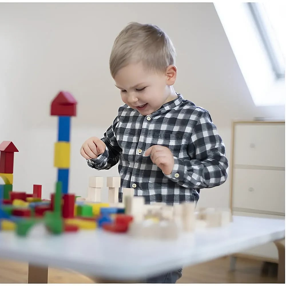 Ein kleiner Junge im karierten Hemd spielt glücklich an einem Tisch mit bunten Holzbauklötzen.
