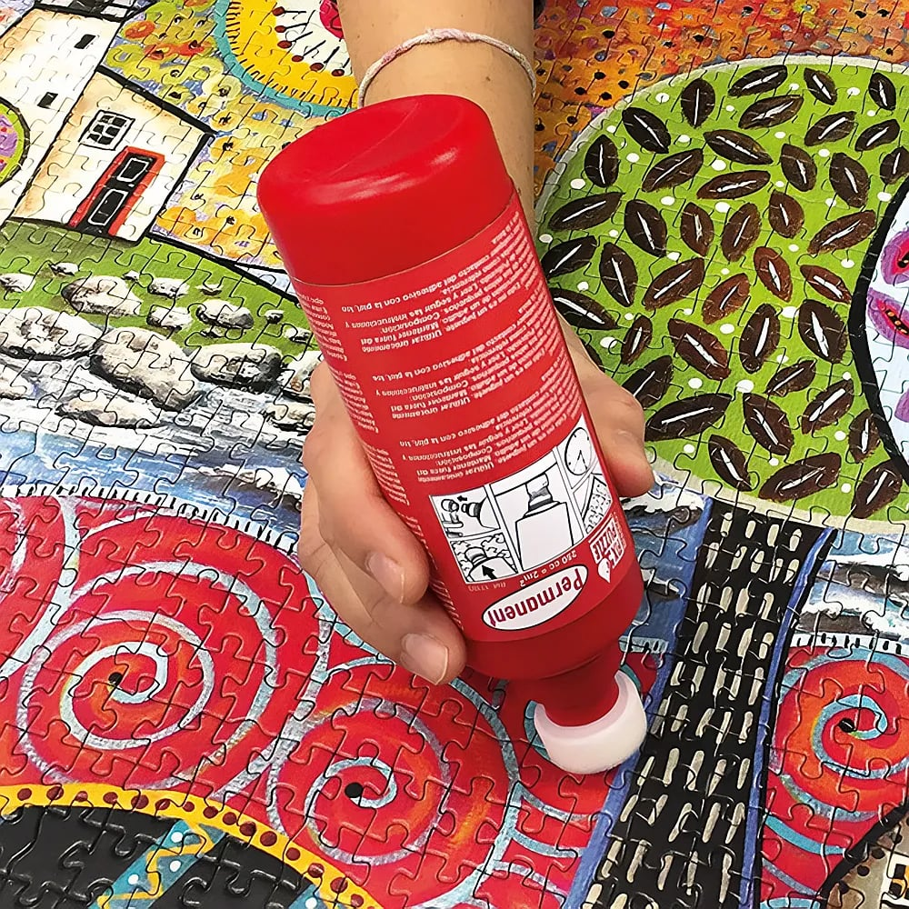 Una mano sostiene un pegamento rojo sobre un colorido puzzle completado.