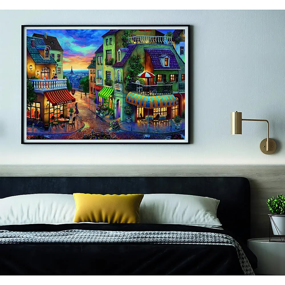 Een kleurrijk schilderij van een Europese straat boven een bed met kussens.