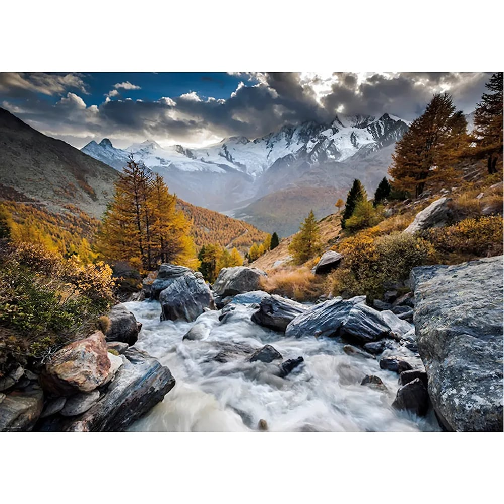 Ein wilder Fluss strömt durch eine herbstliche Berglandschaft mit schneebedeckten Gipfeln und bewölktem Himmel.