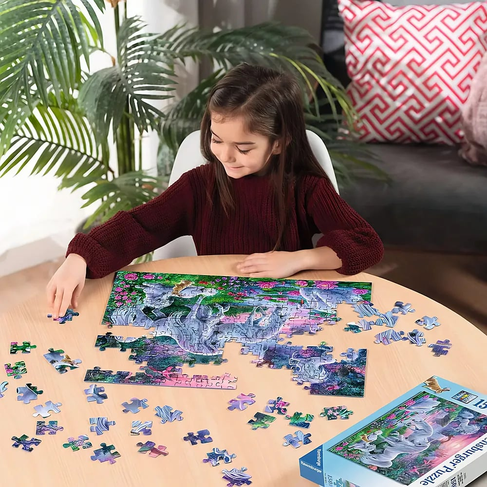 Ein junges Mädchen mit langen braunen Haaren sitzt an einem runden Holztisch und setzt ein buntes Puzzle zusammen.