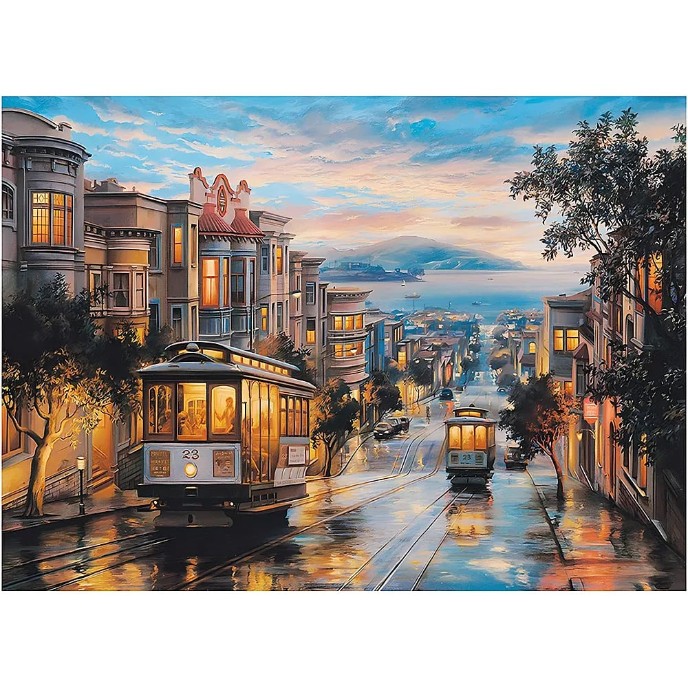 Beleuchtete Straßenbahnen fahren bei Dämmerung auf einer hügeligen Straße in San Francisco mit Blick auf die Bucht.