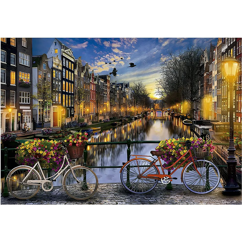 Dos bicicletas con flores en un puente de Ámsterdam al atardecer, con edificios históricos iluminados reflejados.