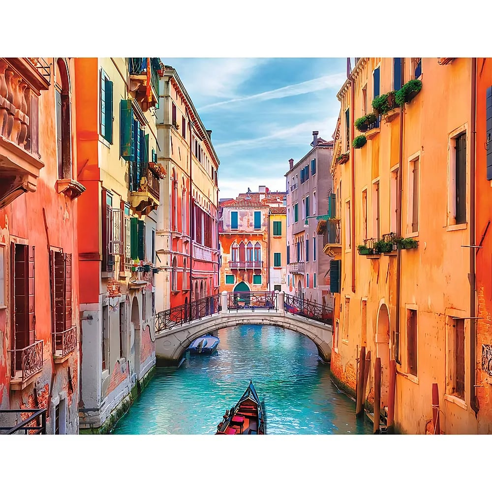 Ein schmaler venezianischer Kanal fliesst unter blauen Himmel zwischen bunten historischen Gebaeuden hindurch.
