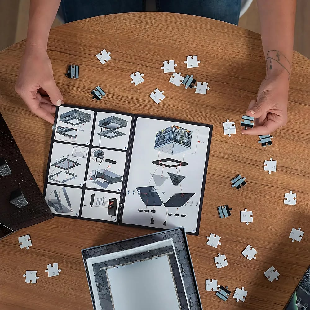 Person sitzt an Holz Tisch und baut ein Puzzle mit Anleitung.