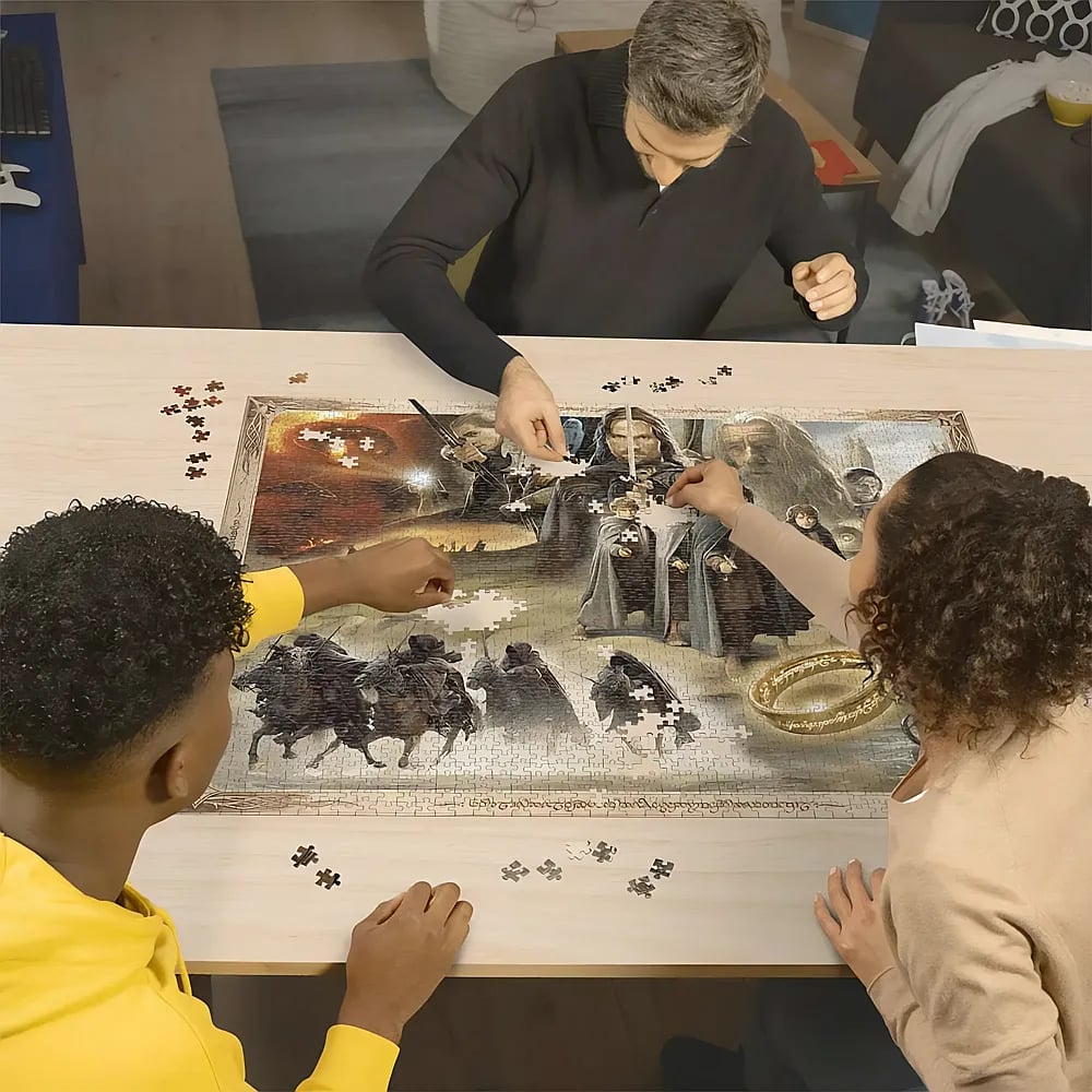 Drei Personen sitzen an einem Holztisch und setzen ein großes Herr-der-Ringe-Puzzle zusammen.