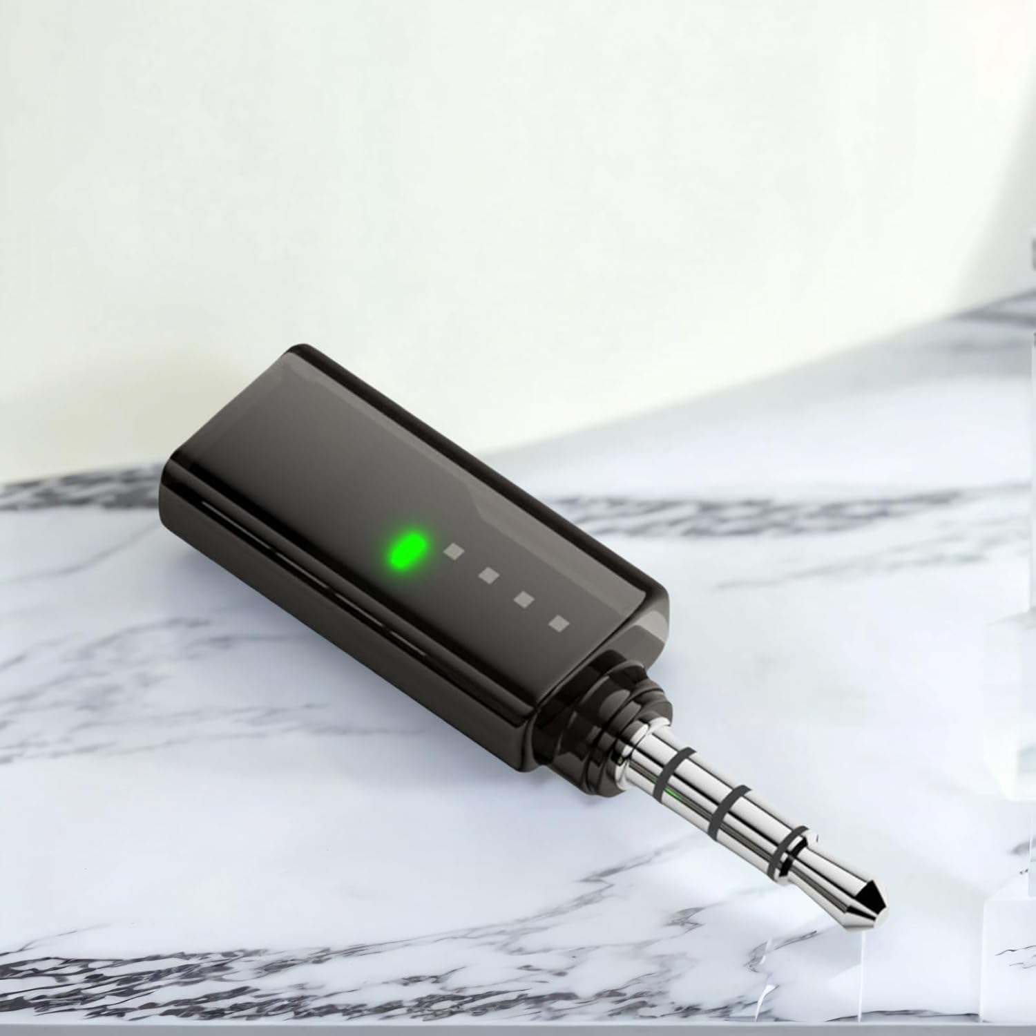 Ein schwarzer Audioadapter mit einem 3,5-mm-Klinkenstecker und einer leuchtenden grünen LED auf einer Marmoroberfläche.