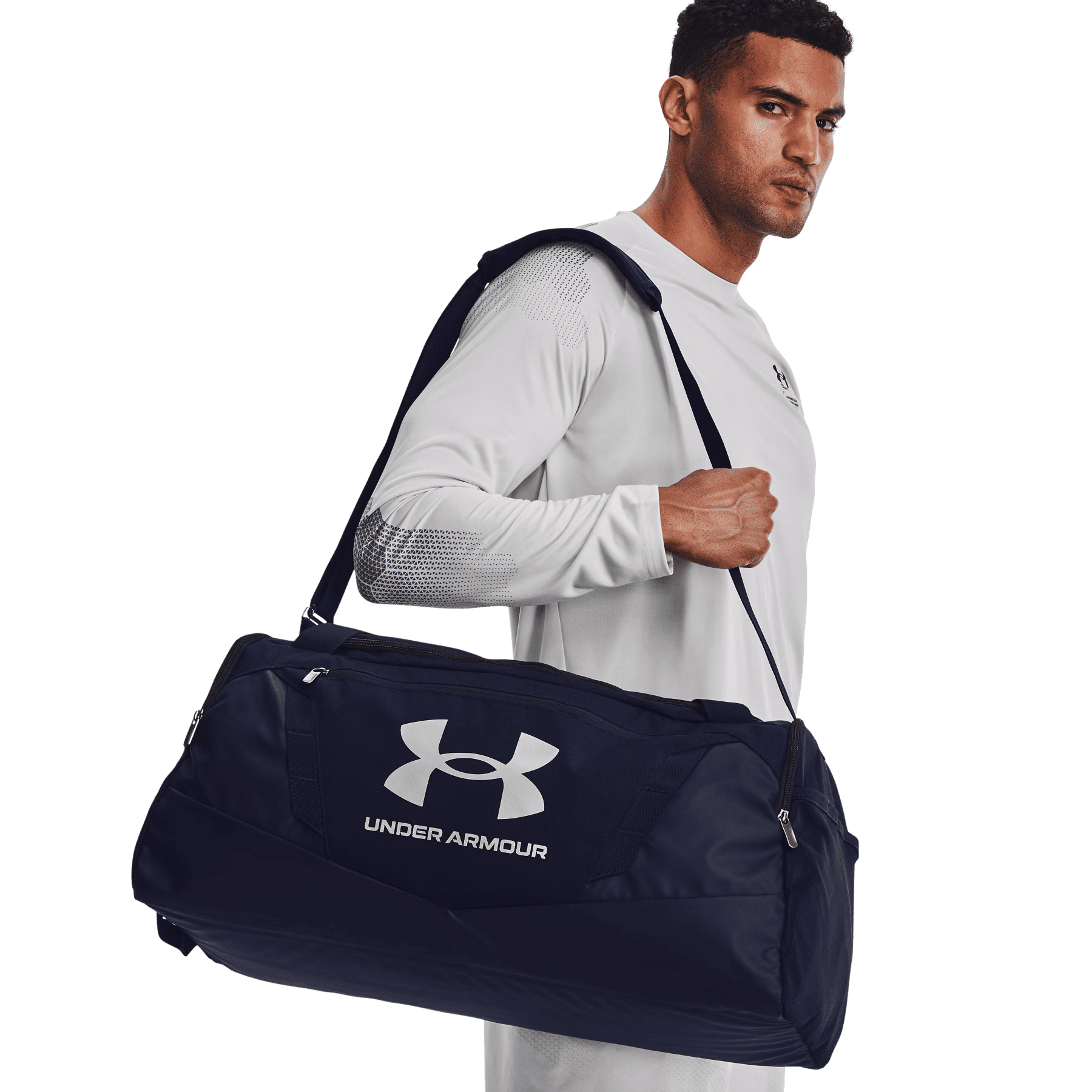 Ein athletischer Mann in weißem Sportshirt trägt eine große blaue Under Armour Sporttasche über der Schulter.