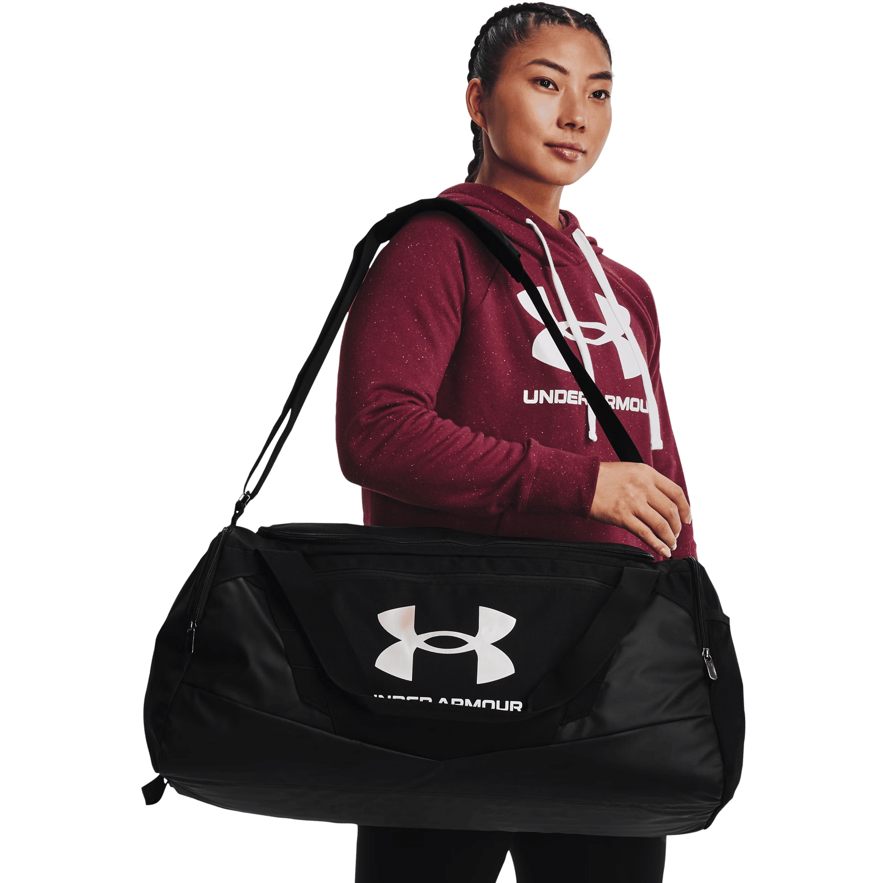 Eine Frau in einem roten Under Armour Hoodie trägt eine schwarze Under Armour Sporttasche vor schwarzem Hintergrund.