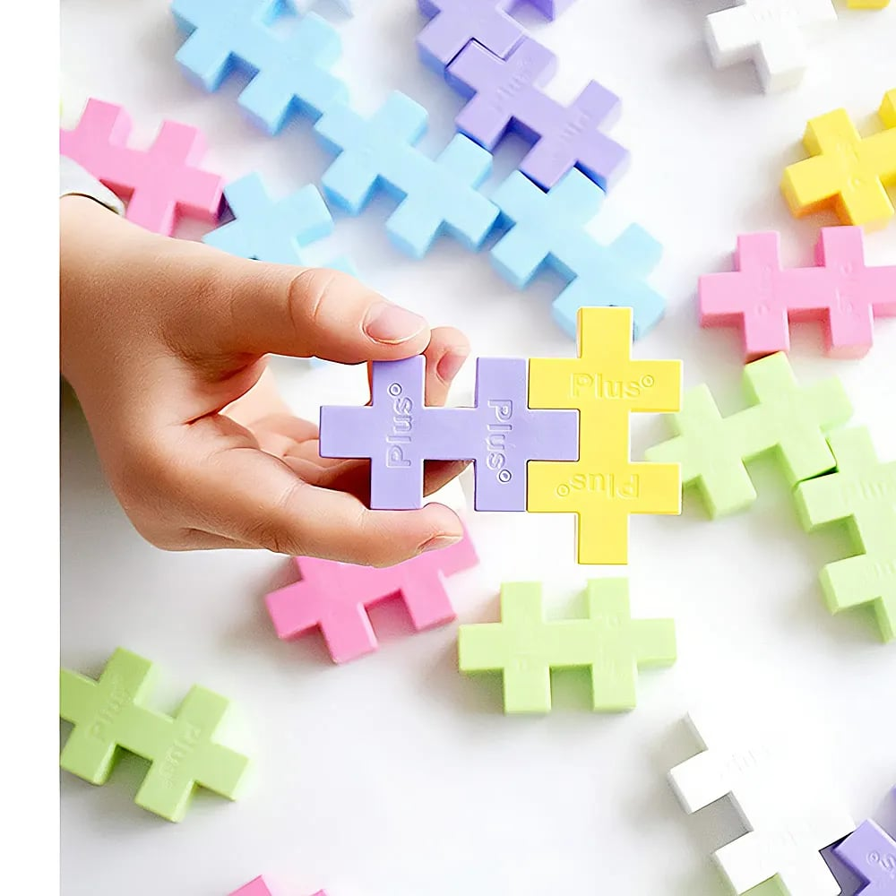 A child's hand holds interlocking pastel-colored puzzle pieces on a white background.