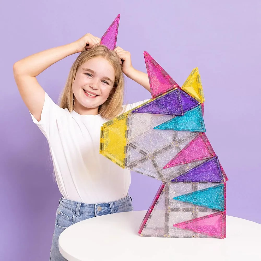 Una ragazza bionda con una maglietta bianca tiene un magico unicorno fatto di piastrelle magnetiche.