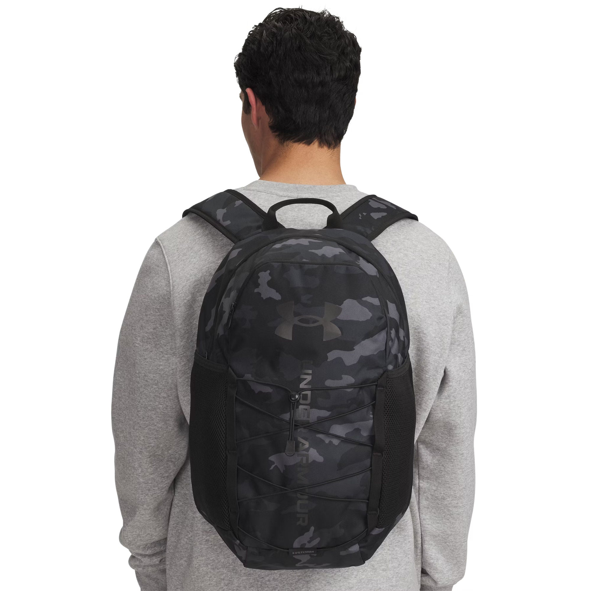 Eine von hinten gezeigte Person trägt einen grauen Pullover und einen schwarzen Tarnrucksack mit Netztaschen.