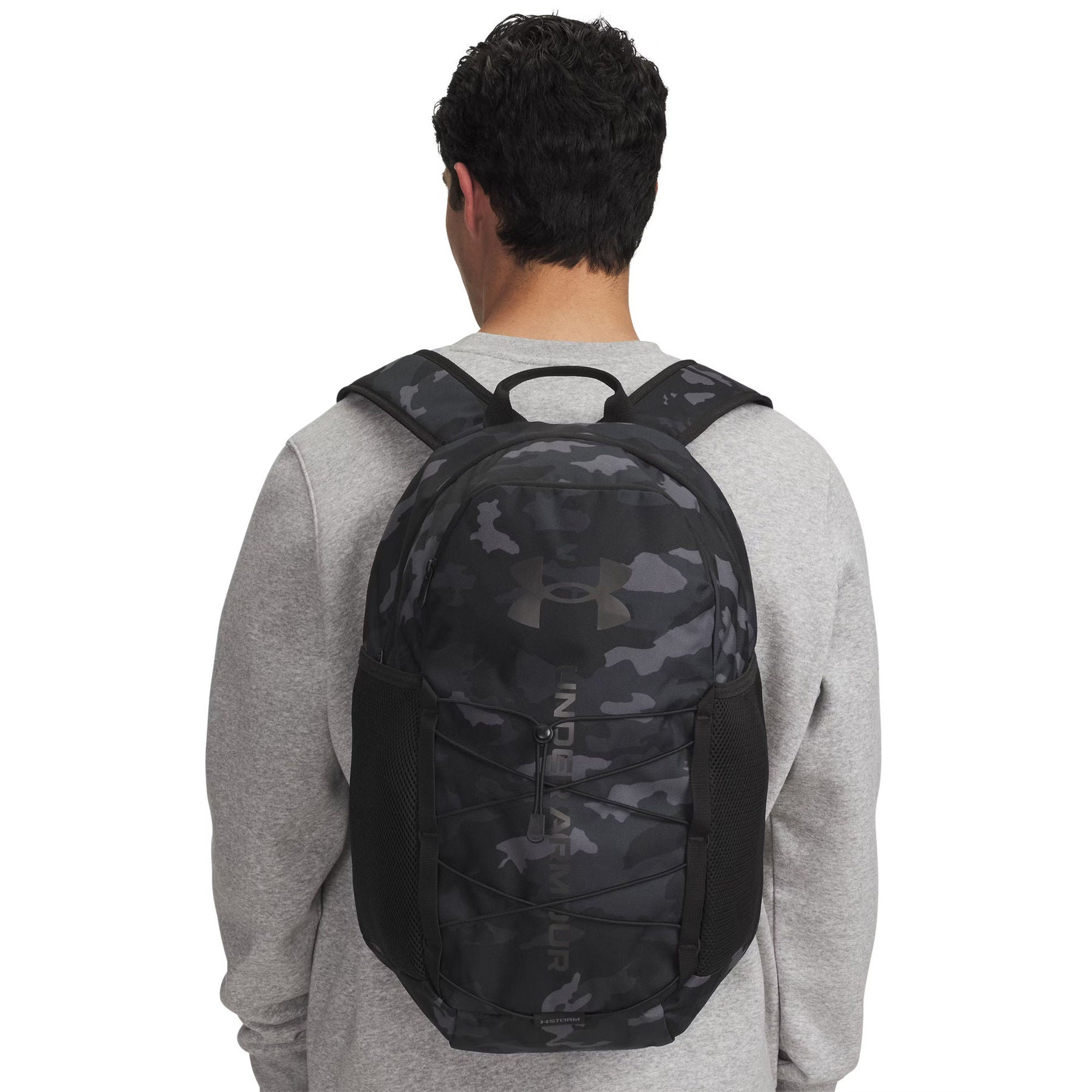 Eine Person von hinten, die einen grauen Pullover und einen schwarz-grauen Tarnmuster-Rucksack trägt.