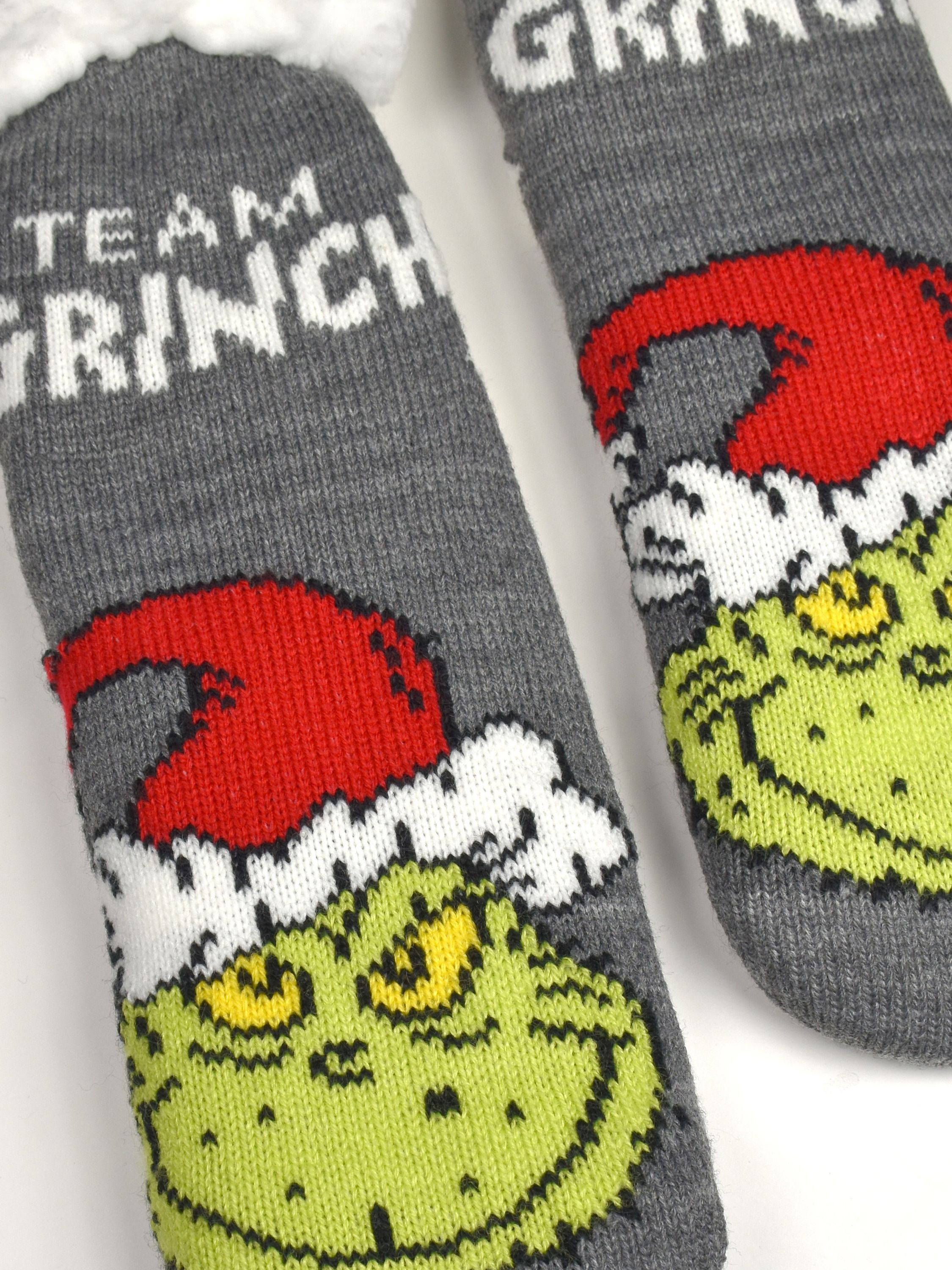 Graue Strickhausschuhe mit Grinch-Motiv und roter Weihnachtsmütze vor weißem Hintergrund.
