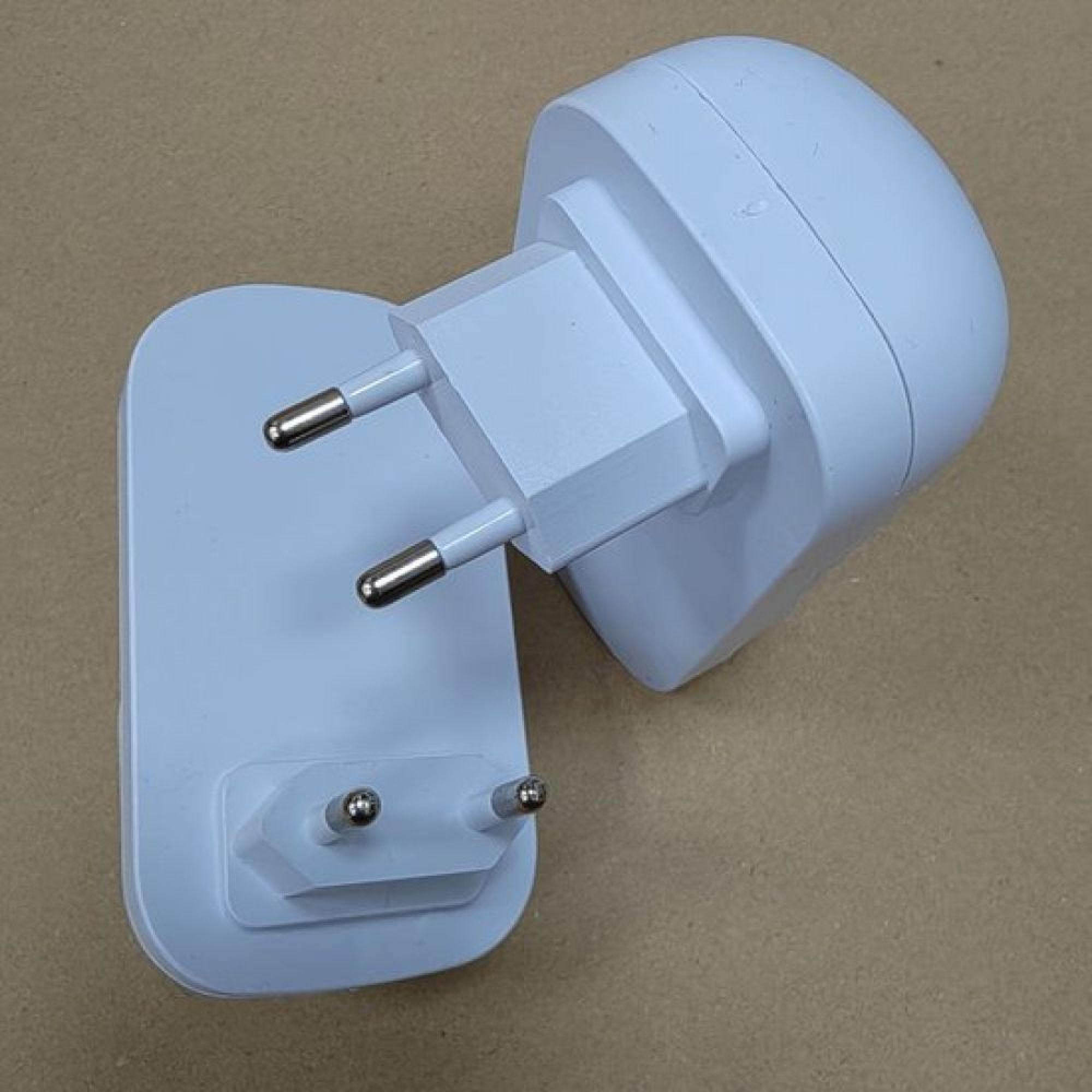 Zwei weiße elektrische Steckdosenadapter mit zwei runden Stiften liegen auf einer braunen Oberfläche.