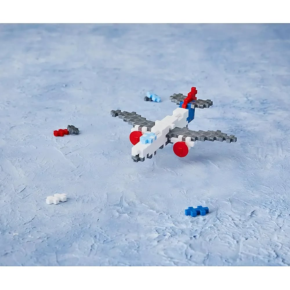 Ein Spielzeugflugzeug aus weißen, grauen, roten und blauen Puzzleteilen auf hellblauem Hintergrund.