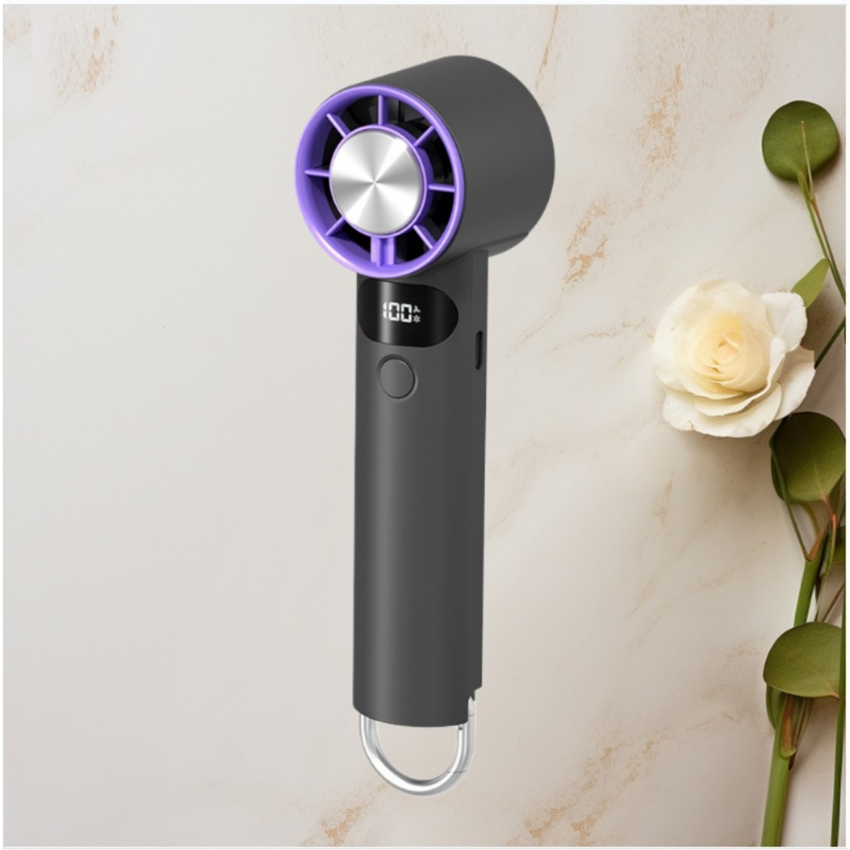 Ein grauer Handventilator mit violetter Umrandung und digitalem Display, platziert neben einer weißen Rose auf Marmor.