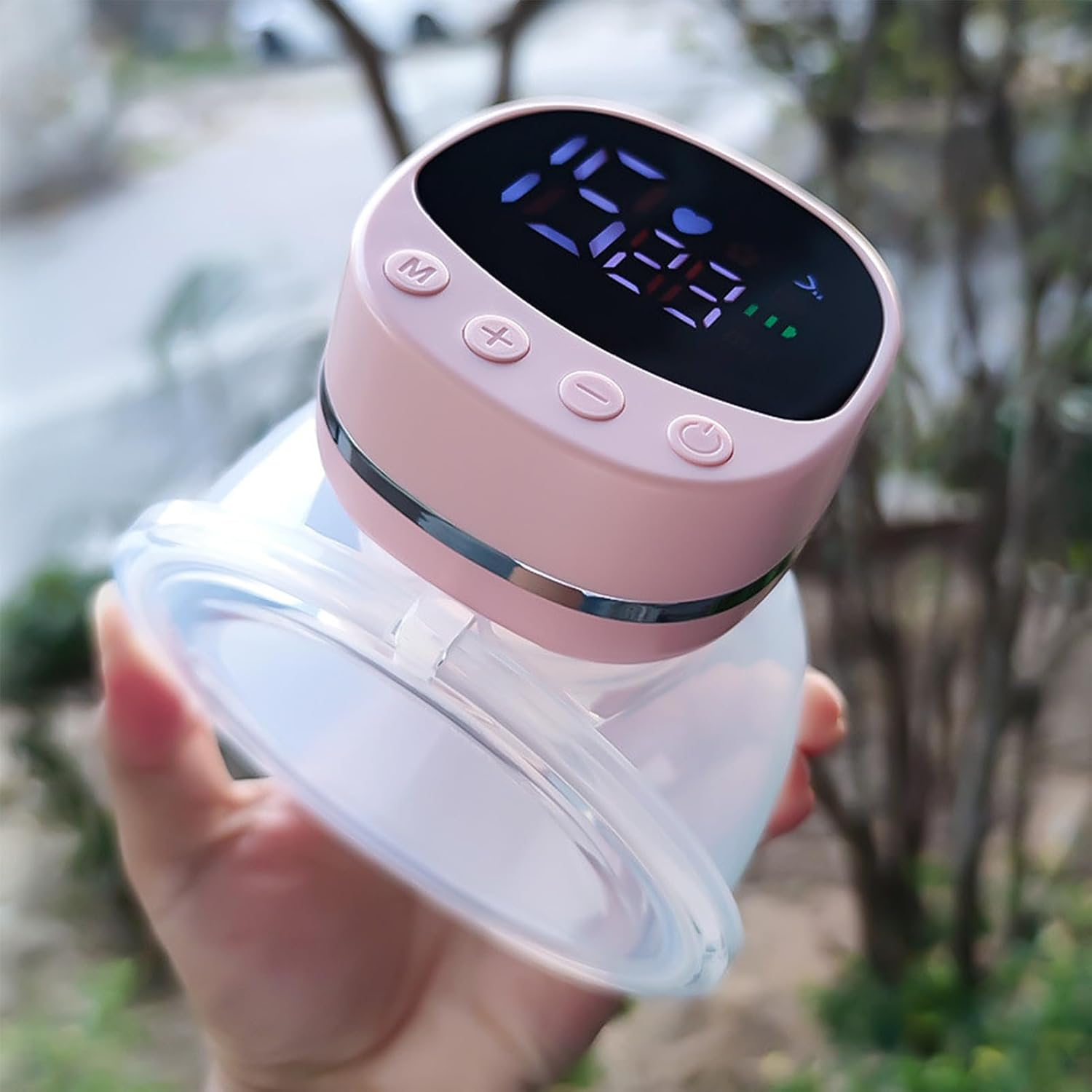 Eine Hand hält eine rosa und transparente elektrische Milchpumpe mit Digitaldisplay im Freien.