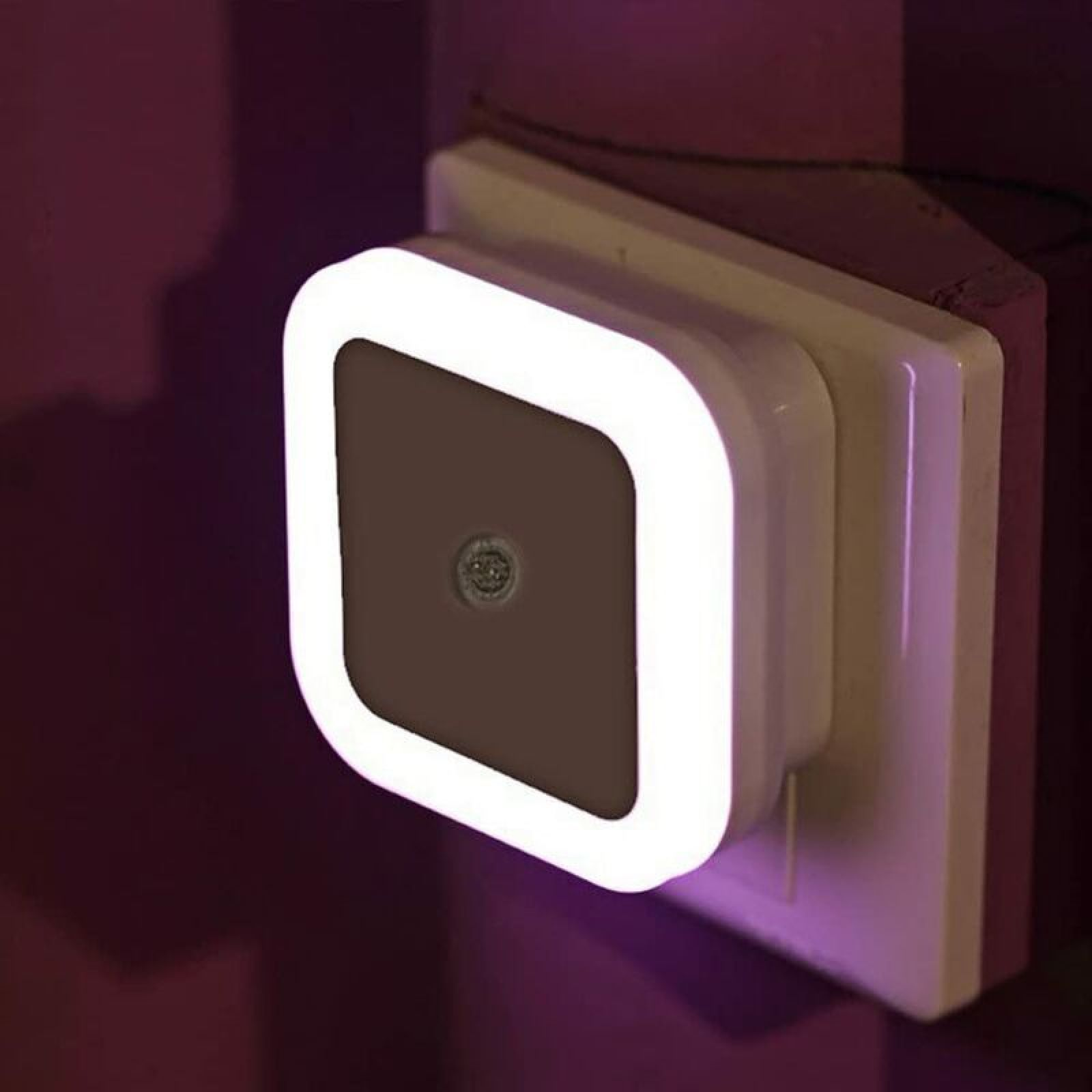 Eine quadratische weiße LED-Nachtleuchte mit hellem Rand steckt in einer Steckdose an einer Wand.