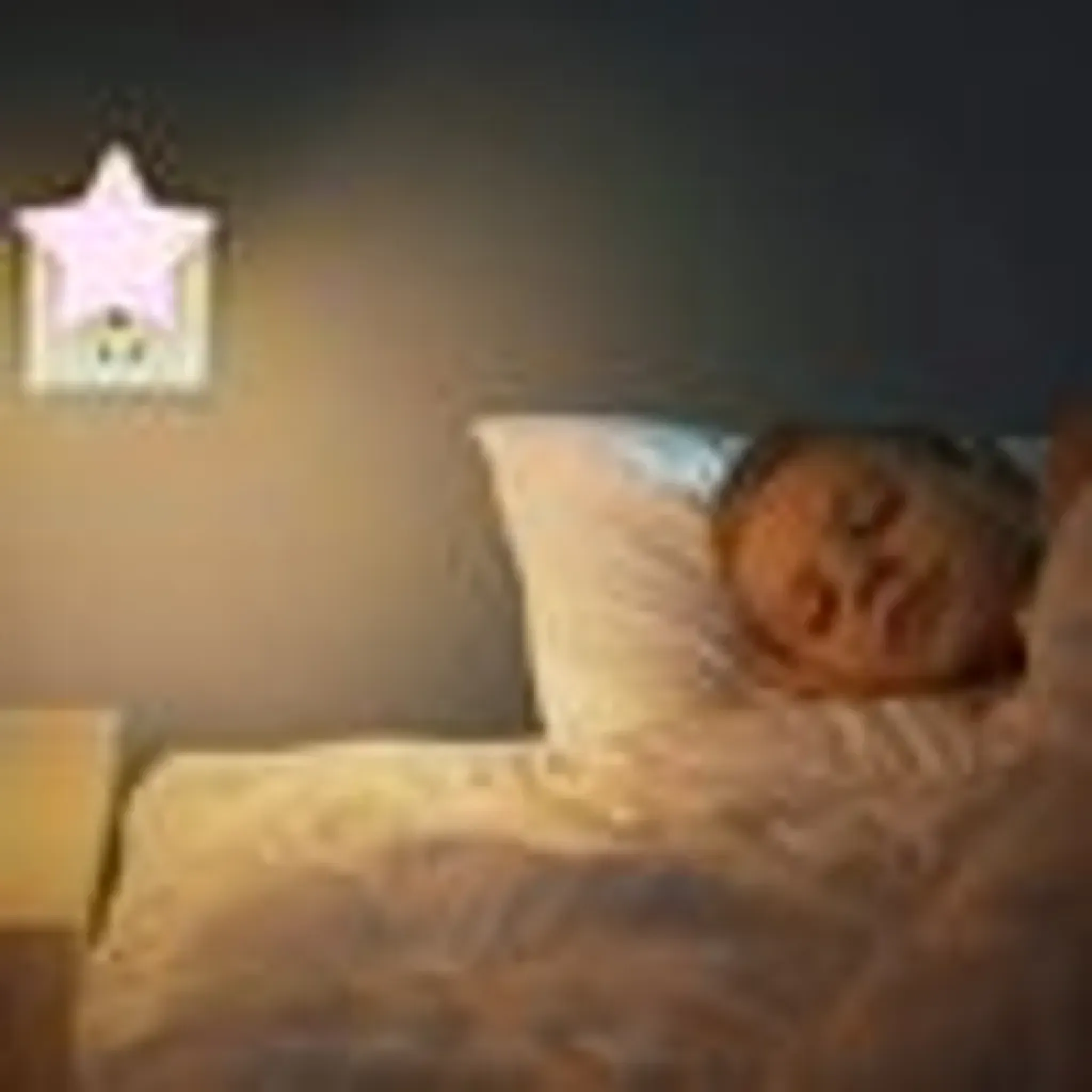 Ein Kind schläft friedlich im Bett, beleuchtet von einem sternförmigen Nachtlicht an der Wand.