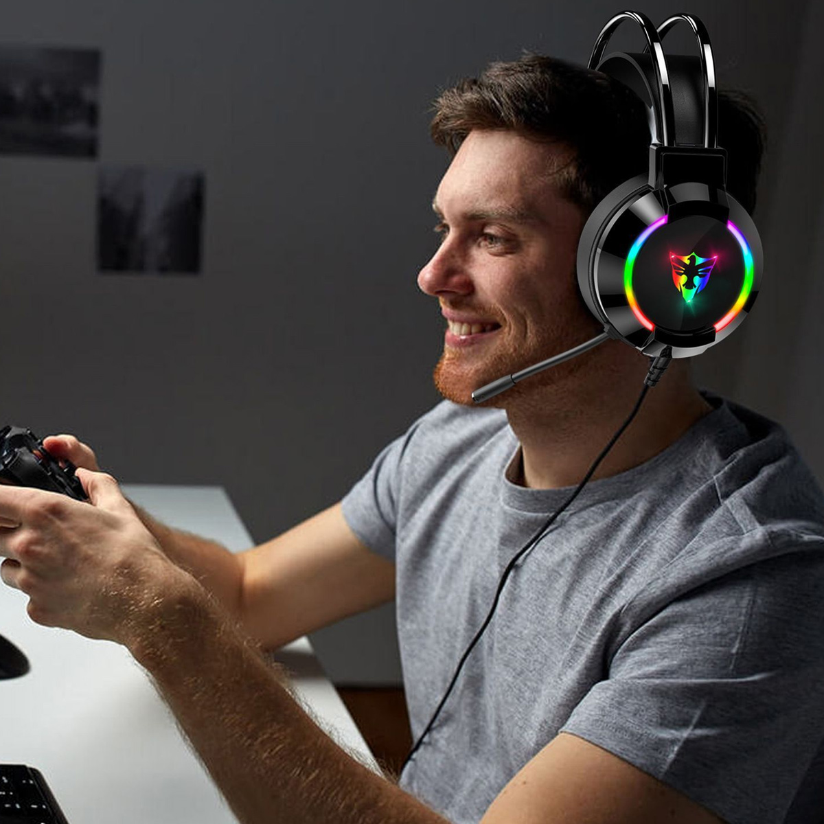 Mann mit grauem Shirt trägt leuchtende Gaming-Kopfhörer und hält einen Controller.