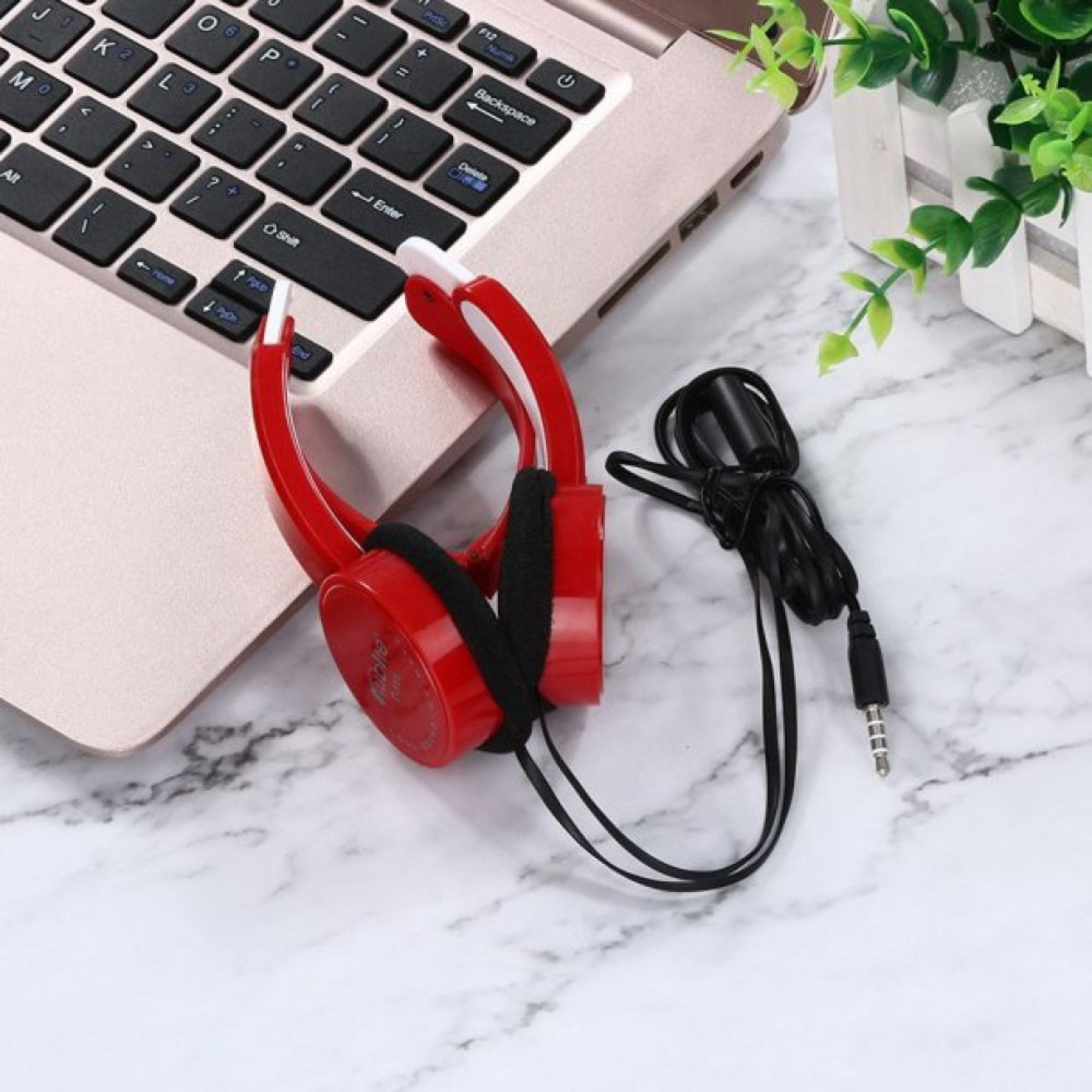 Rote Kopfhörer und ein schwarzes Kabel liegen neben einem Laptop auf einem Marmortisch.