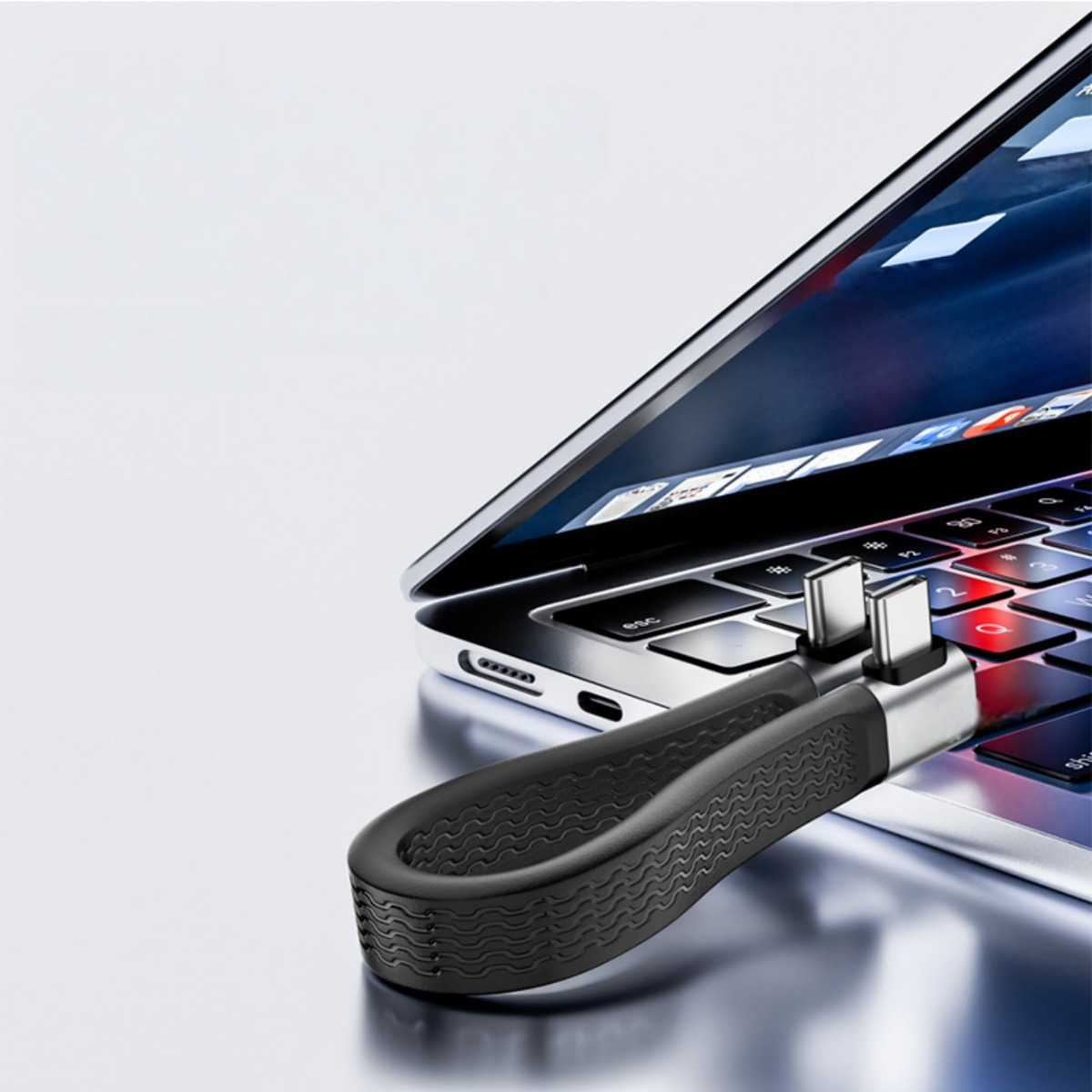 Ein schwarz-silberner USB-C-Adapter mit integrierter Schlaufe liegt auf einer Laptop-Tastatur.