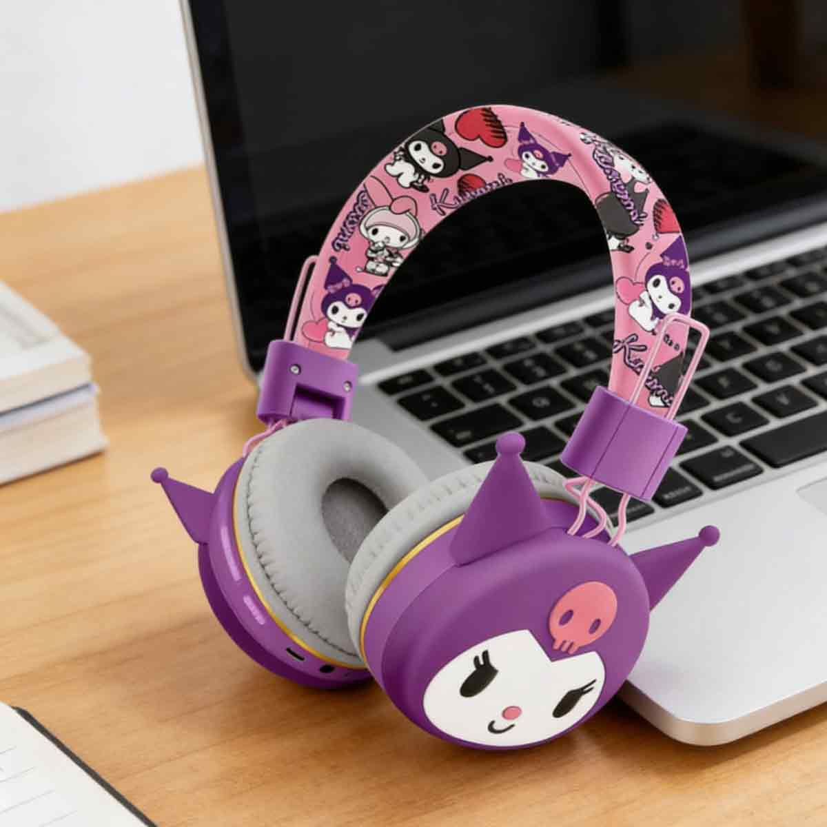 Lila, rosa Kuromi-Kopfhörer mit Ohren liegen auf einem Laptop auf einem Holztisch.