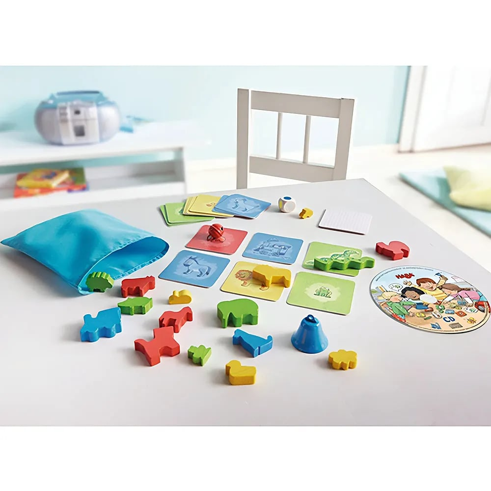 Colorato gioco per bambini su un tavolo con carte, figure di animali in legno, una borsa blu e una campanella.