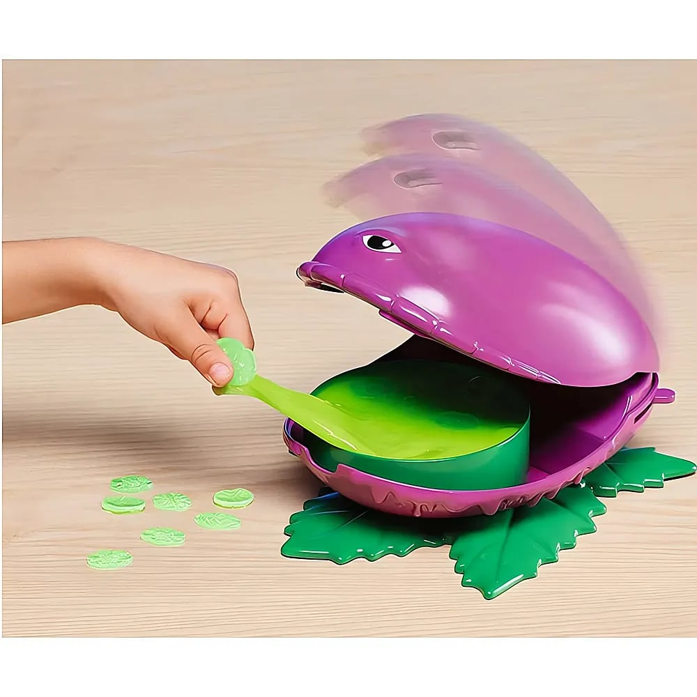 Ein Kind füttert ein lila Pflanzenspielzeug mit grünem Schleim auf der Zunge, neben kleinen grünen Marken auf einem Holztisch.