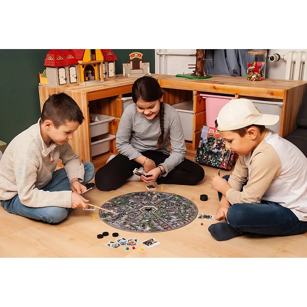 Drei Kinder spielen ein Brettspiel auf dem Holzboden in einem Kinderzimmer.