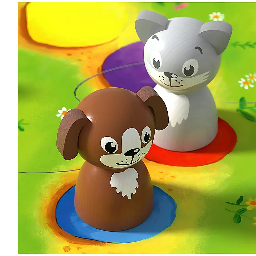 Holzfiguren von Hund und Katze auf einem bunten Spielbrett mit grünem Hintergrund.