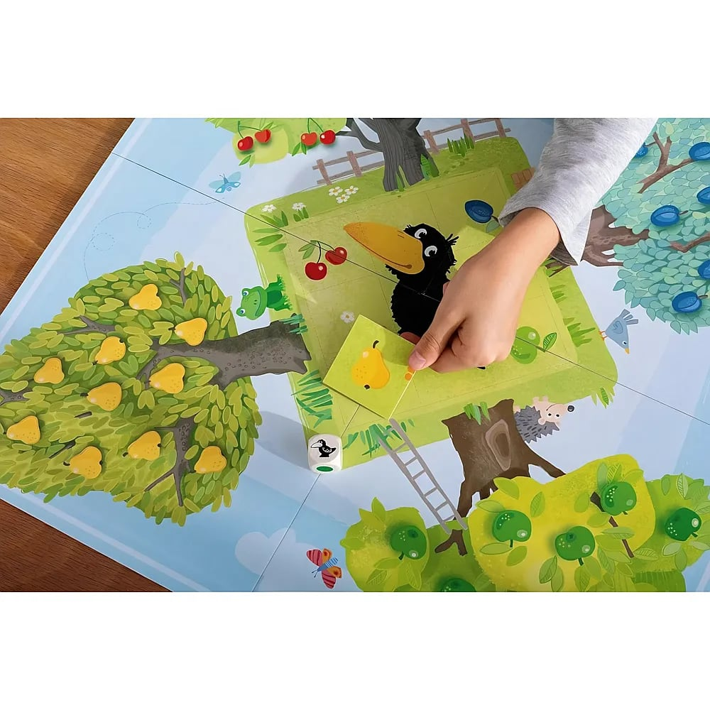 Ein Kind spielt ein Obstgarten-Brettspiel und legt eine Birnenkarte in die Nähe eines Raben.