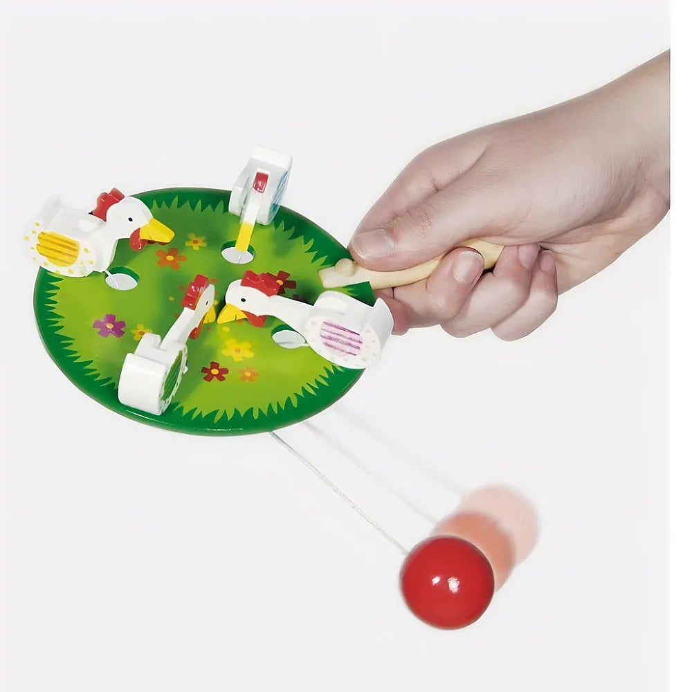 Eine Hand bedient ein grünes Holzspielzeug mit Hühnern und einer roten Pendelkugel.