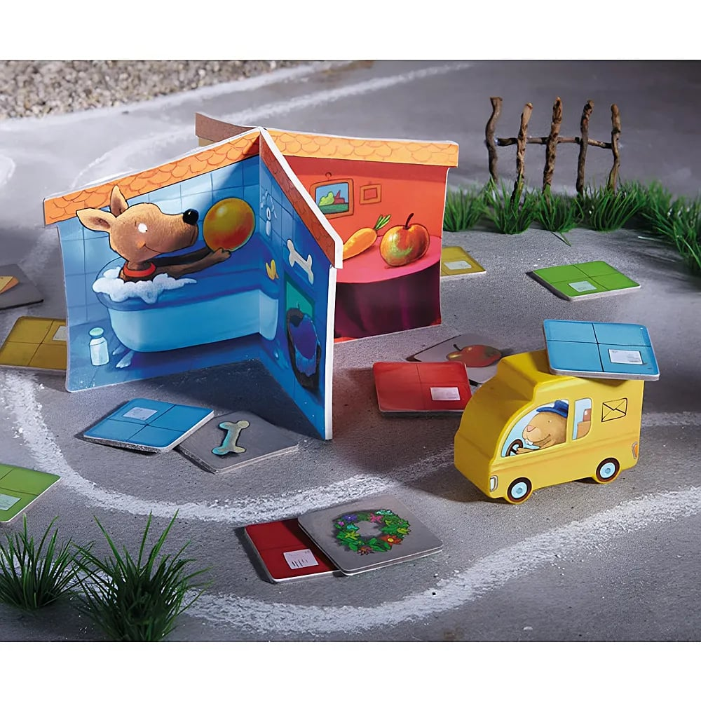 Un jeu en carton avec un chien dans une baignoire, un camion postal jaune et des carreaux colorés au sol.
