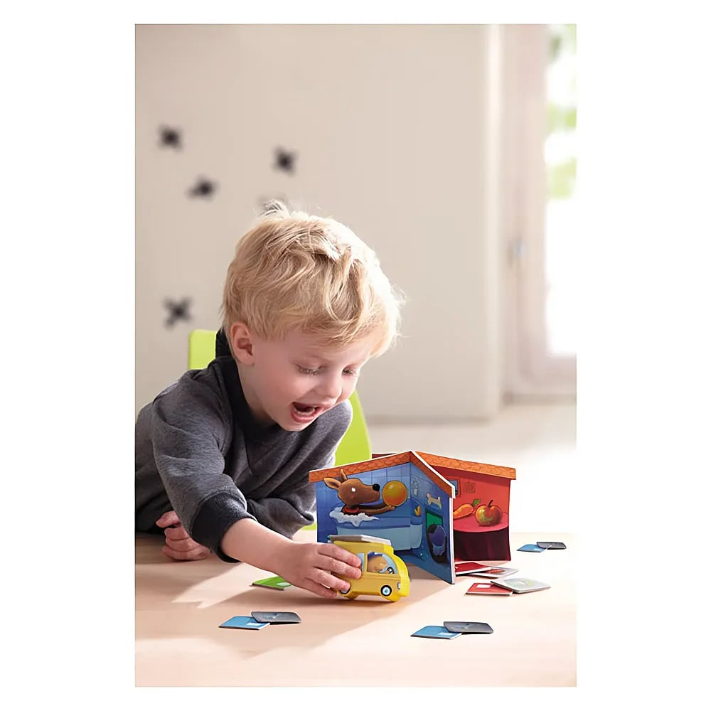 Jeune garçon assis à une table jouant joyeusement avec une voiture jouet jaune et une maison en carton.