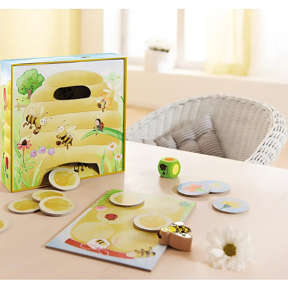 Kinderspiel mit Bienen-Thema auf einem Holztisch, inklusiv Box, Würfel, Spielbrett und runden Holzteilen.