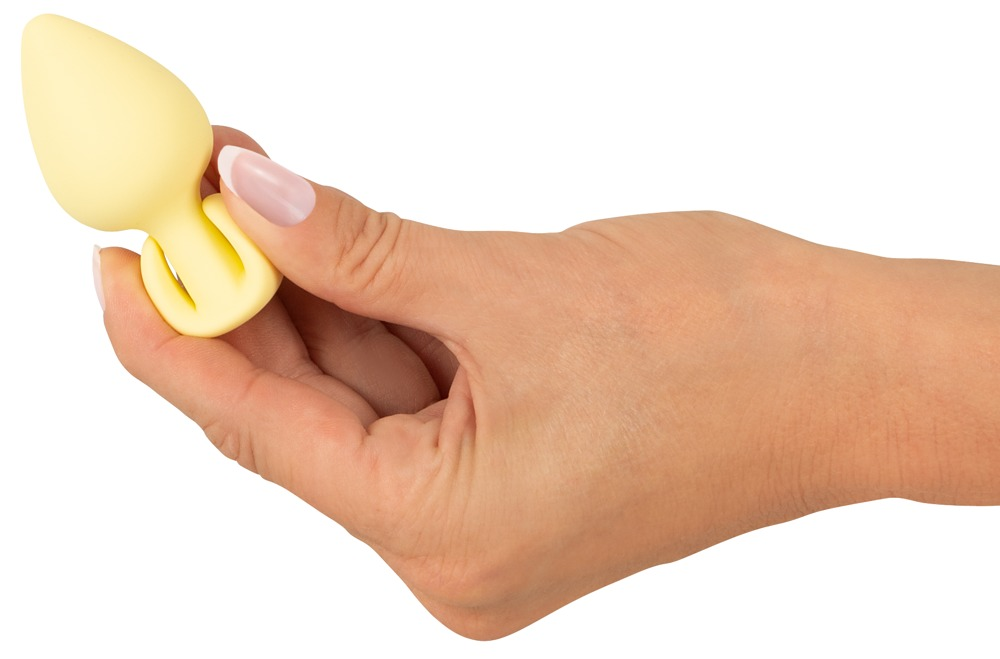 Eine Hand hält einen gelben, tropfenförmigen Wellnessartikel vor einem weißen Hintergrund.