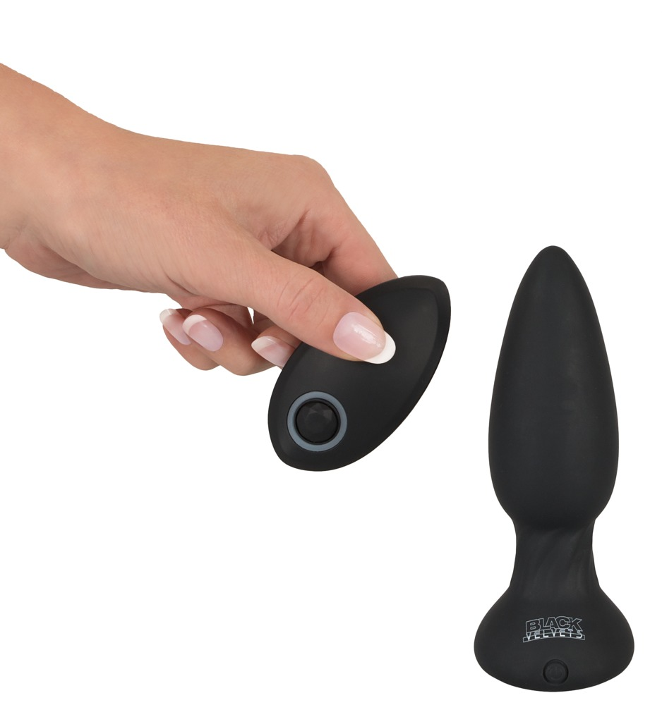 Eine Hand hält eine schwarze ovale Fernbedienung neben einem schwarzen Butt Plug auf weißem Hintergrund.
