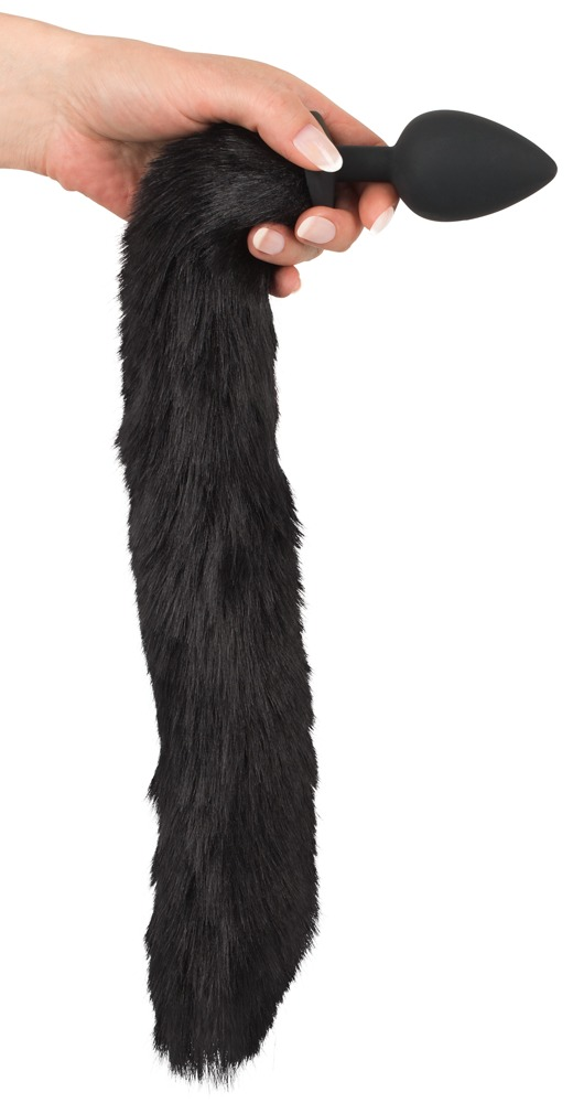 Eine Hand hält einen schwarzen Buttplug mit einem langen, flauschigen schwarzen Kunstfell-Schwanz daran.