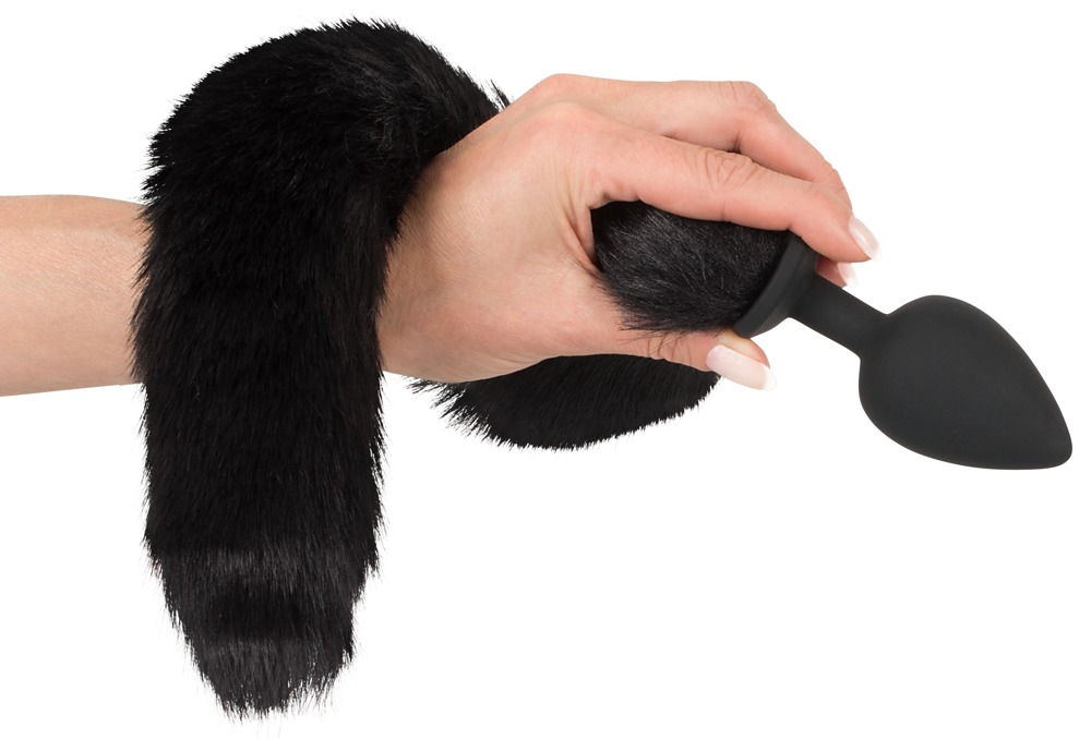 Eine Hand hält einen schwarzen Flauschschwanz an einem glatten schwarzen Stopfen vor weißem Hintergrund.