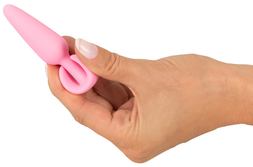 Eine Hand hält ein kleines, rosafarbenes Wellness-Accessoire mit einer spitz zulaufenden Form gegen weißen Hintergrund.