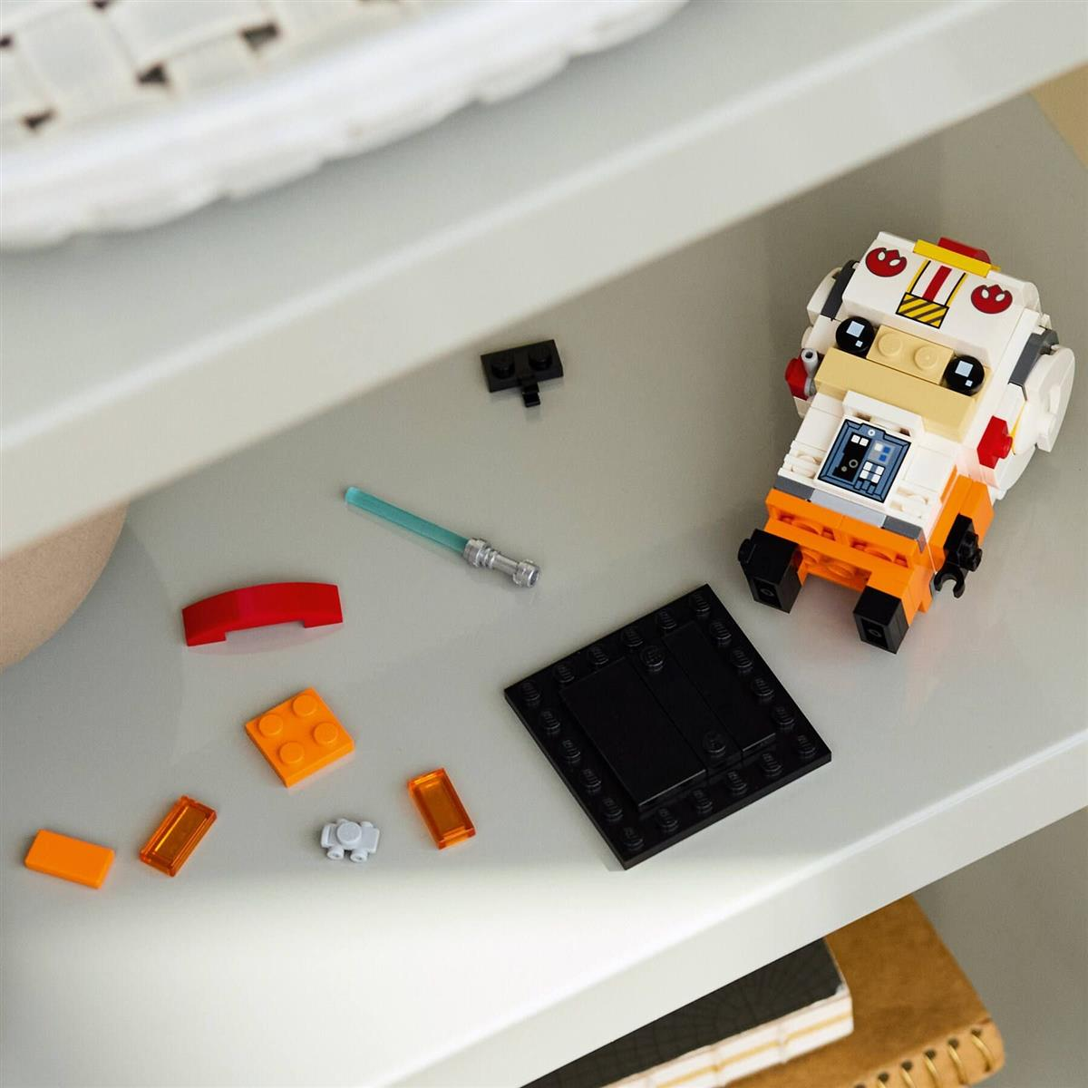 Eine Lego Star Wars Figur mit kleinen losen Lego-Teilen und einem Lichtschwert auf einem Regal.